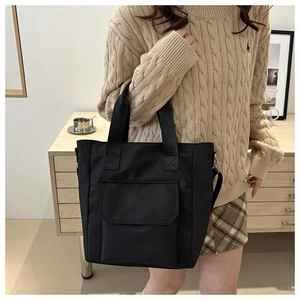 Close-up of a black large capacity tote bag with front pocket held by a model in a knit sweater
