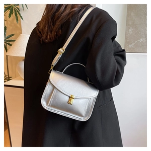 Sac messager en cuir argenté mat avec fermoir doré, porté par un mannequin en intérieur