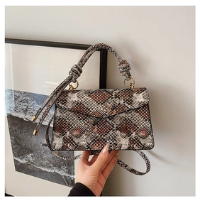 Detail of snake skin pattern handbag with knotted handle and gold metal rings