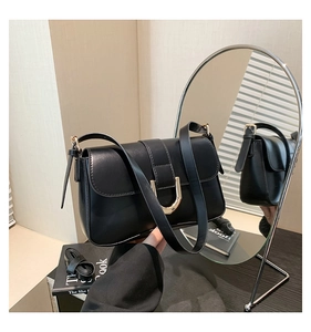 Detail of black faux leather underarm bag with gold horseshoe buckle and smooth finish