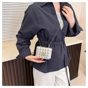 Detail of silver quilted mini crossbody bag with star emblem worn over a blue shirt