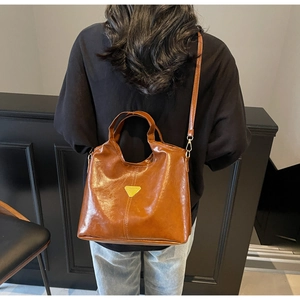 Brown glossy leather bucket bag with gold triangle logo on a person showing bag size