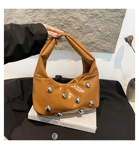 Close-up of caramel leather shoulder bag featuring silver metal rivets and pleated texture