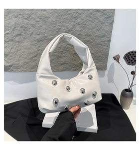 Detail of white glossy patent leather handbag featuring large silver metal stud accents