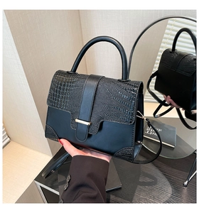 Detail view of black handbag showing crocodile pattern flap and smooth leather texture
