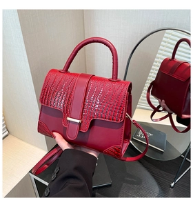 Detail of red faux crocodile skin texture and gold buckle on a stylish crossbody bag
