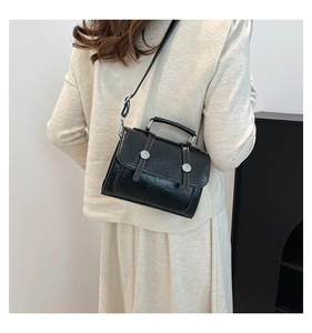 Close-up of vintage black glossy leather crossbody bag with silver buckles and handle