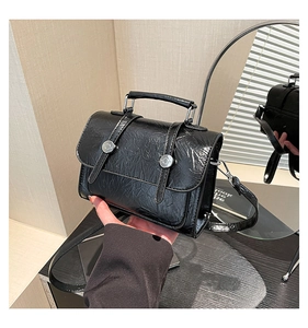 Detail of black pleated faux leather handbag with silver metallic buckle and top handle