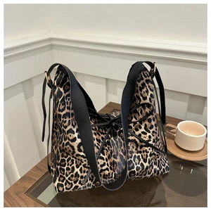 Détail du sac cabas léopard avec lanière noire et nœud décoratif sur une table en bois