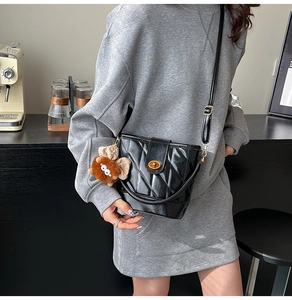Detail of black quilted bucket bag with gold clasp and plush charm on a shoulder strap