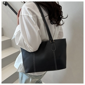 Detail view of a black tote bag featuring distinctive white contrast stitching on leather