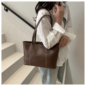Detail of a brown tote bag with white contrast stitching on a model in a minimalist setting