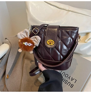 Detail of burgundy quilted bucket bag with golden twist lock and plush monster charm