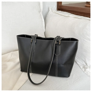 Close-up of a black tote bag with white contrast stitching and gold hardware detail