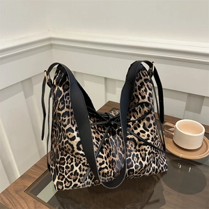 Grand sac cabas à motif léopard avec anses en cuir noir et nœud décoratif sur une table en bois