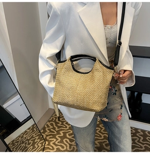 Detail of woven straw tote bag with black leather straps styled on a fashion model
