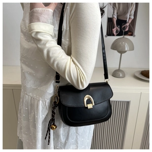 Detail of a black leather saddle bag with gold horseshoe buckle and decorative charm