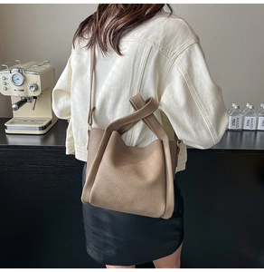Detail of beige litchi grain leather bucket bag with FASHION embossment and crossbody strap