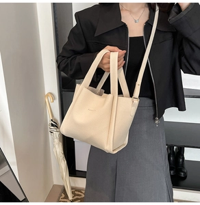 Detail of a beige lychee pattern bucket bag with FASHION logo and adjustable strap
