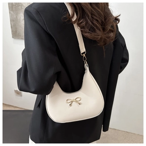 Detail of white baguette bag with golden bow ornament on a black blazer background