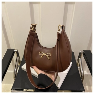 Close-up of brown hobo bag featuring a decorative gold metal bow and smooth finish