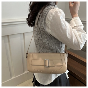 Side view of beige baguette bag with silver buckle worn by a model in a minimalist setting