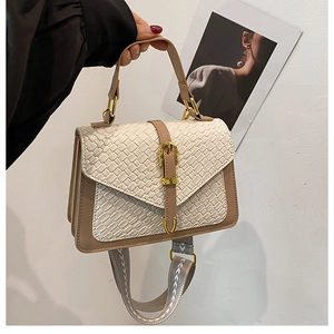 Detail of a brown leather crossbody bag with beige woven texture and wide floral strap