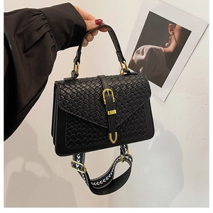 Detail of black crossbody bag featuring woven texture flap and geometric embroidered strap
