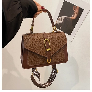 Detail of dark brown woven texture handbag with gold buckle and chic geometric strap