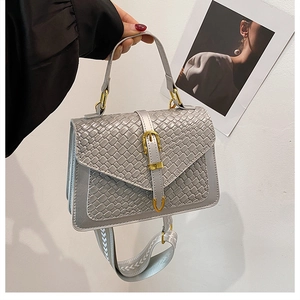 Close-up of grey handbag with woven texture flap, golden buckle and patterned shoulder strap