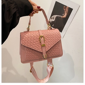 Close-up of pink woven leather handbag with metallic buckle and wide patterned shoulder strap