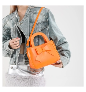 Detail einer leuchtend orangefarbenen Umhängetasche mit großer Schleife am Denim-Outfit