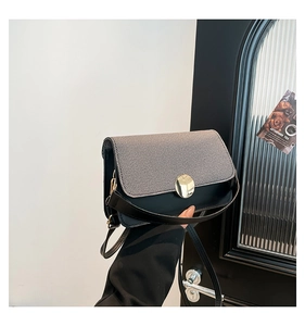 Detail of a two-tone crossbody bag featuring grey twill texture and a gold metal clasp