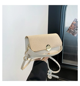 Detail of crossbody square bag featuring straw texture flap and large gold round buckle