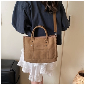 Detail of tan canvas tote bag with metal rivets and shoulder strap on model back