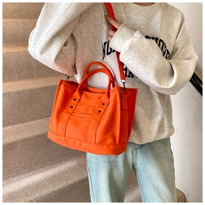 Detailed view of orange canvas tote bag with webbed handles and detachable shoulder strap