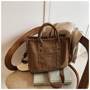 Detail view of large canvas tote bag with decorative rivets on a wooden chair