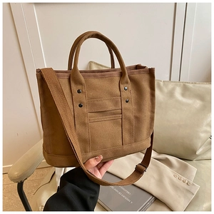 Close-up of brown canvas tote bag with adjustable strap and rivet details in a cozy setup