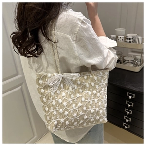 Detail of floral embroidery and white lace bow on the woven straw tote bag
