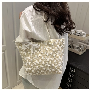 Close-up of beige straw tote bag with white flower embroidery and lace bow details