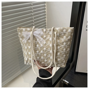 Detail of woven tote bag featuring white floral embroidery and a lace bow charm