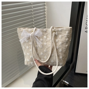 Close-up of beige straw tote bag featuring floral embroidery and white lace bow detail