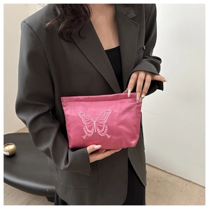 Close-up of rose pink satin pouch with elegant butterfly embroidery held by a model