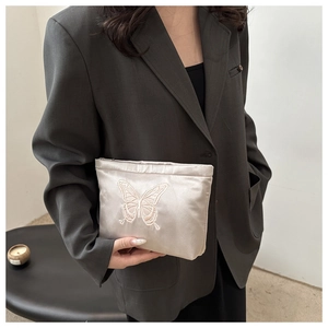 Detailed view of champagne satin clutch featuring butterfly embroidery held by a model