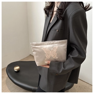 Detail of champagne satin clutch with butterfly embroidery held by a model in a suit