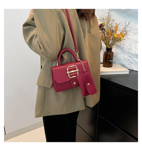 Detail of burgundy leather handbag set with litchi texture and gold metal buckle strap