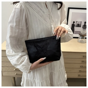 Detailed view of butterfly embroidery on black satin clutch held by model in white dress