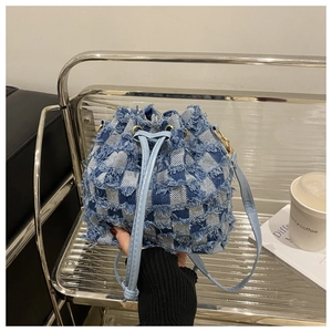 Détail du sac seau en denim bleu avec motif à damier et bords à franges fins