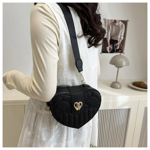 Detail of black heart quilted crossbody bag with gold metal clasp and wide strap