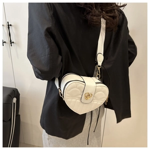 Detail of white quilted heart crossbody bag with gold metallic lock and wide strap